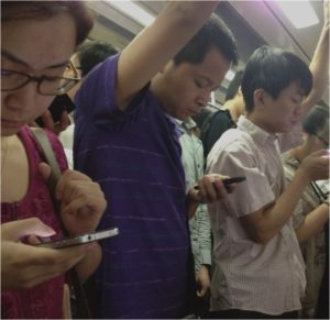 A bunch of Asian looking people on a train looking at their mobile phone screens